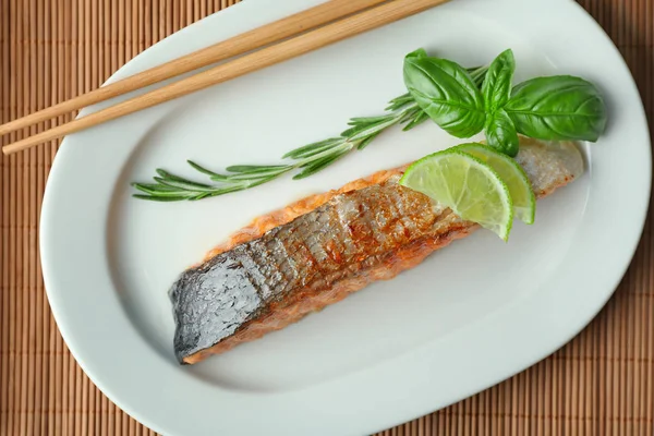 Plate with slice of delicious salmon and chopsticks on table — Stock Photo, Image