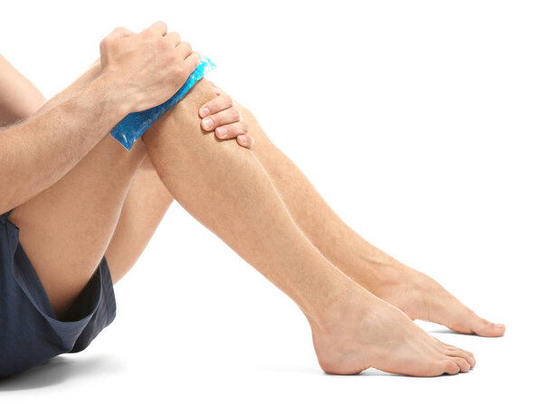 Young man applying cold compress to leg on white background