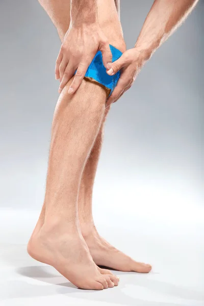 Junger Mann kalte Kompresse auf Bein vor hellem Hintergrund — Stockfoto