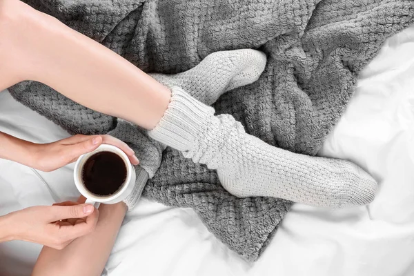 Jonge vrouw in sokken op bed met kopje koffie — Stockfoto