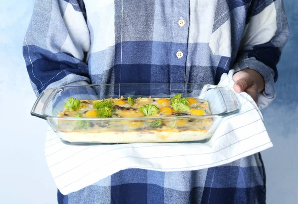 Mujer sosteniendo bandeja para hornear con cazuela de brócoli sobre fondo claro — Foto de Stock