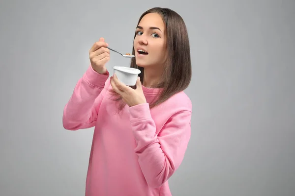 Young woman eating yogurt on light background — Stock Photo, Image