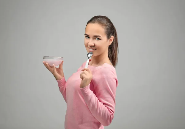 Ung kvinna äta yoghurt på ljus bakgrund — Stockfoto