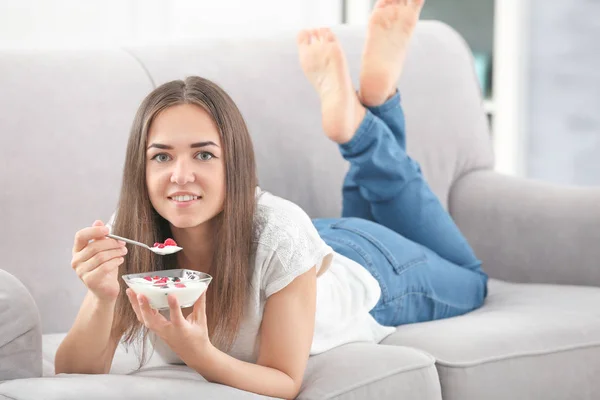 Jovem mulher comendo iogurte no sofá em casa — Fotografia de Stock