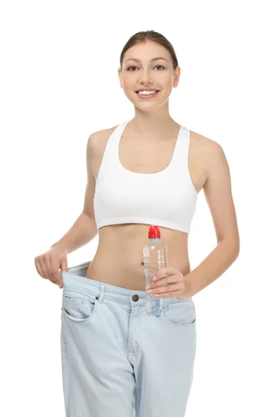 Όμορφη νεαρή γυναίκα με υπερμεγέθη τζιν με μπουκάλι νερό σε άσπρο φόντο. Διατροφή έννοια — Φωτογραφία Αρχείου