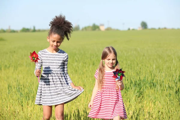Gelukkig weinig meisjes met speelgoed windmolens in groene veld — Stockfoto