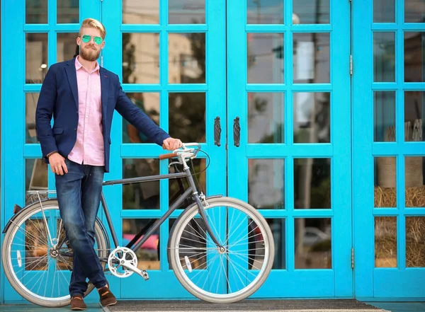 Joven hombre guapo con bicicleta de pie cerca de las ventanas —  Fotos de Stock