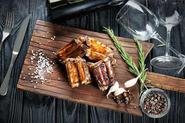 Wooden board with delicious ribs on table