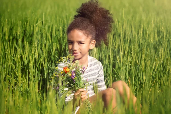 Little Afro American girl with bouquet of wildflowers in green field — Stock Photo, Image