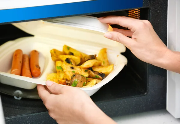 Akşam yemeği ile plastik konteyner mikrodalga fırına koyarak kadın. Bir kavram için pişirme