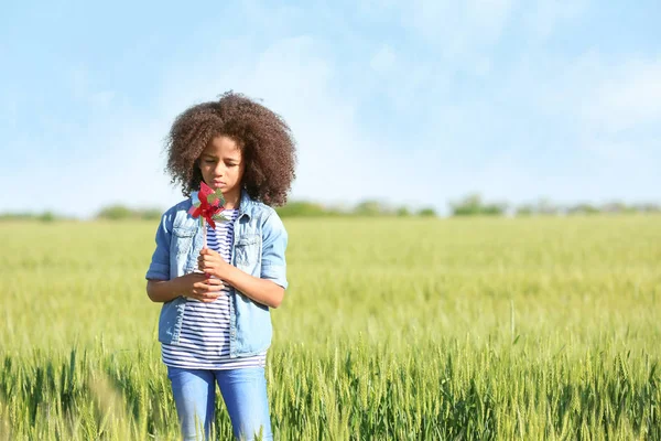 Kleines afroamerikanisches Mädchen mit Spielzeugwindrad im grünen Feld — Stockfoto