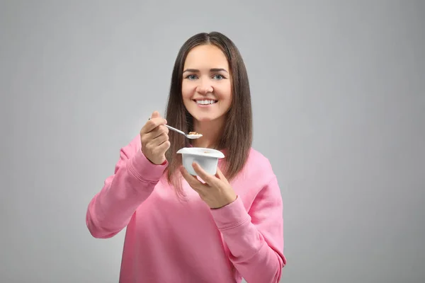 Ung kvinna äta yoghurt på ljus bakgrund — Stockfoto