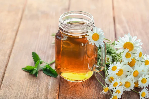 Mason jar of chamomile tea with flowers on wooden background — Stock Photo, Image