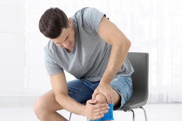 Young man applying cold compress to leg at home