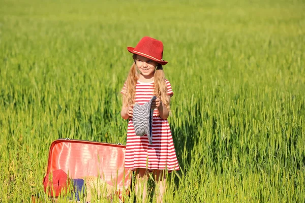 Liten flicka med resväska i grönt fält — Stockfoto