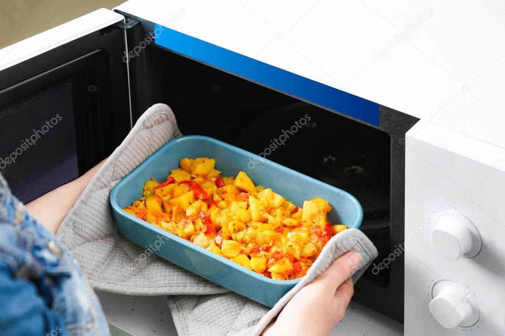 Woman taking out baking dish with dinner from microwave oven. Cooking for one concept