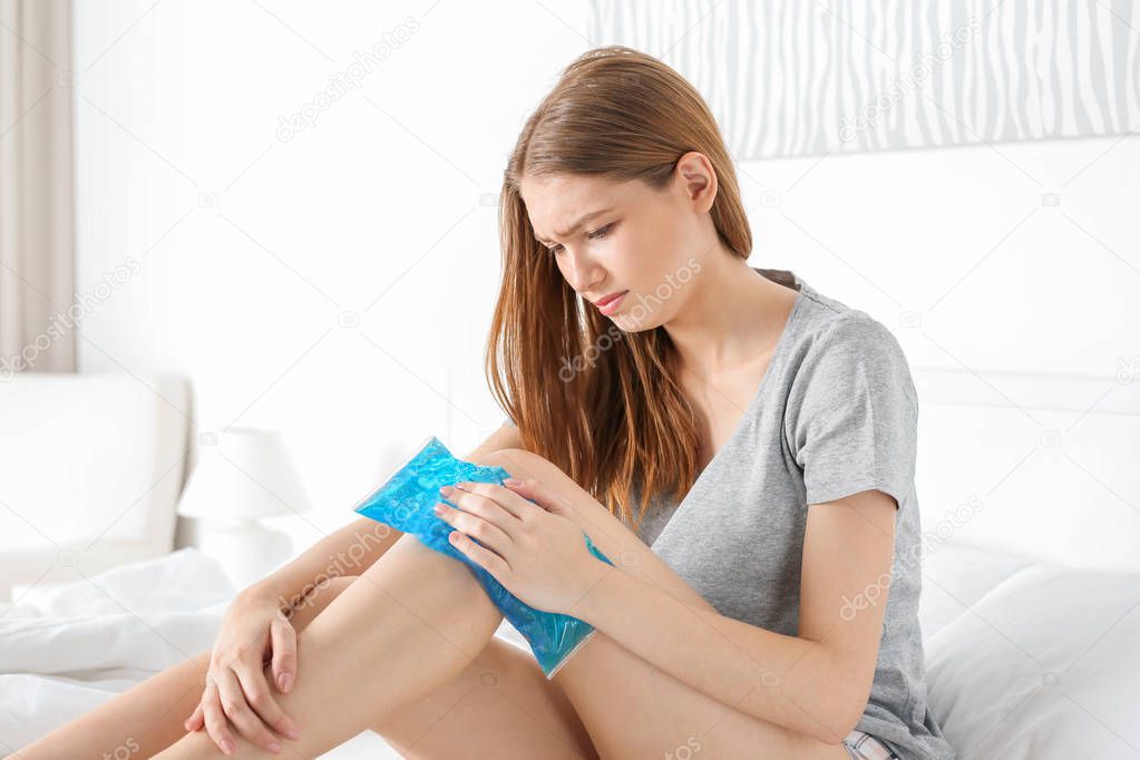Young woman applying cold compress to leg at home