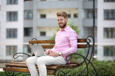 Açık havada bankta oturan dizüstü bilgisayar ile genç blogger