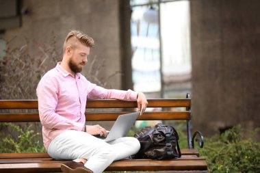 Açık havada bankta oturan dizüstü bilgisayar ile genç blogger