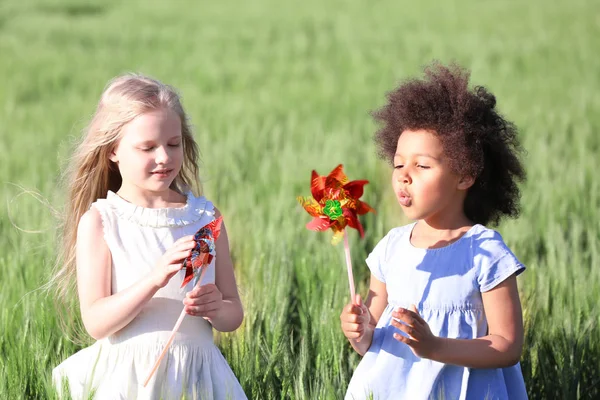 Niñas felices con molinos de viento de juguete en el campo verde — Foto de Stock