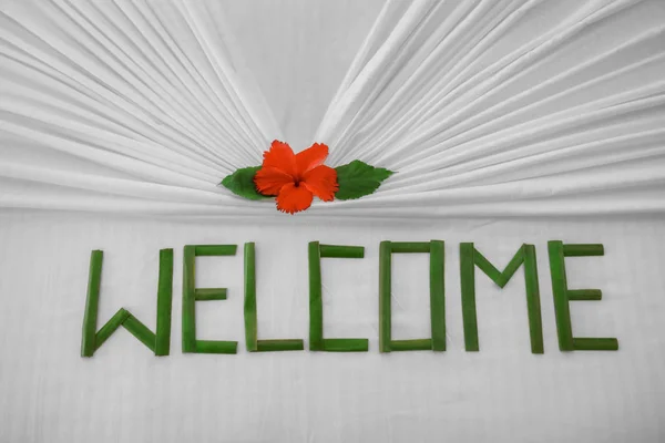 Floral decor and word WELCOME on bed in hotel room, closeup — Stock Photo, Image