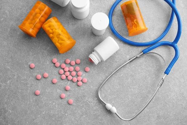 Plastbeholdere med piller og stetoskop på grått bord – stockfoto