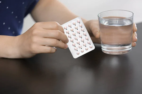 Woman with birth control pills and glass of water at table