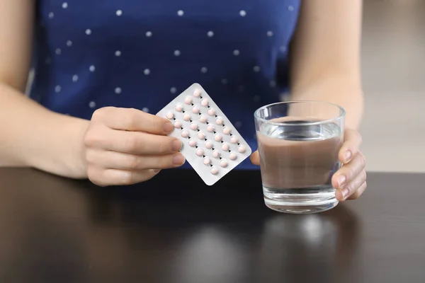 Mujer con píldoras anticonceptivas y vaso de agua en la mesa — Foto de Stock