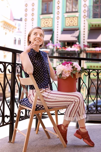 Belle jeune fille assise sur une chaise avec des fleurs de pivoine dans une boîte-cadeau, à l'extérieur — Photo