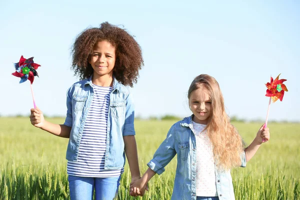 Niñas felices con molinos de viento de juguete en el campo verde —  Fotos de Stock