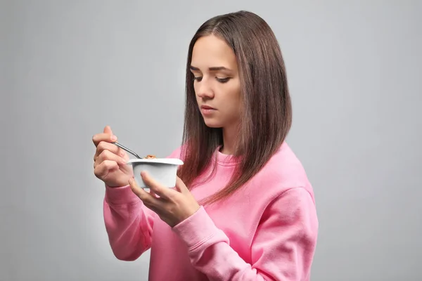 Ung kvinna äta yoghurt på ljus bakgrund — Stockfoto