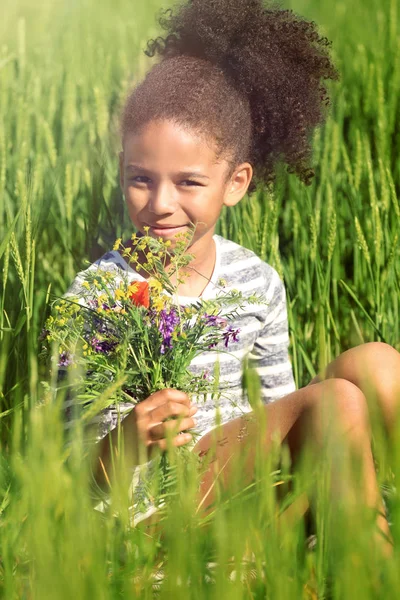 Kleines afroamerikanisches Mädchen mit einem Strauß Wildblumen im grünen Feld — Stockfoto