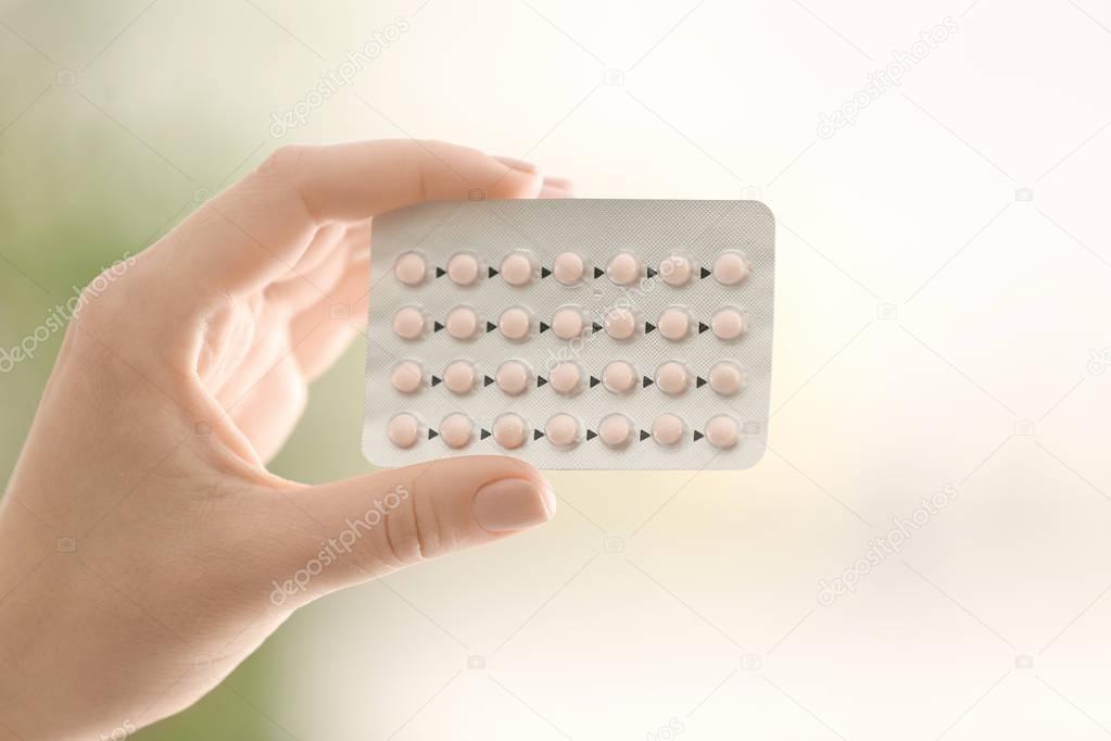 Female hand with hormonal pills on blurred background
