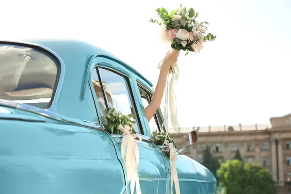 Gyönyörű fiatal menyasszony csokor gazdaság díszített autó szabadban — Stock Fotó