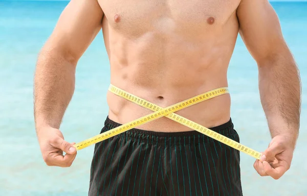 Joven guapo midiendo su cintura en la playa del mar — Foto de Stock