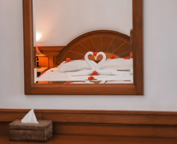Bed with towel swans and floral decor reflecting in hotel room mirror — Stock Photo, Image