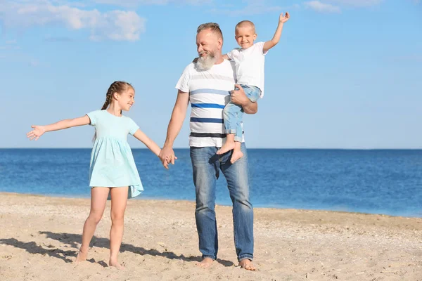 Cute children with grandfather on sea beach — Stock Photo, Image