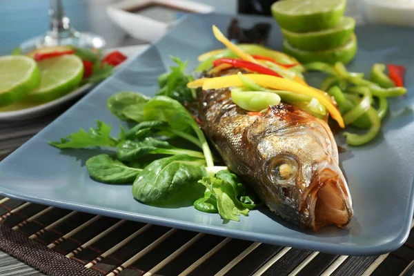 Serving plate with delicious fish in sauce and garnish on table