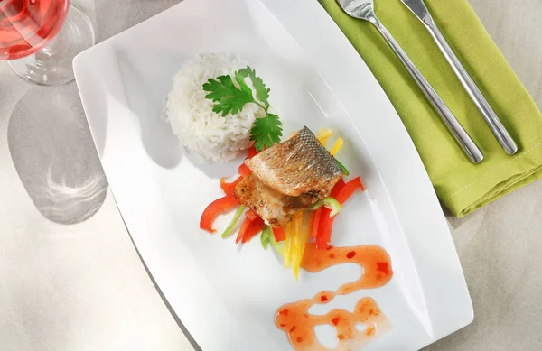 Serving plate with delicious fish, sauce, rice and vegetables