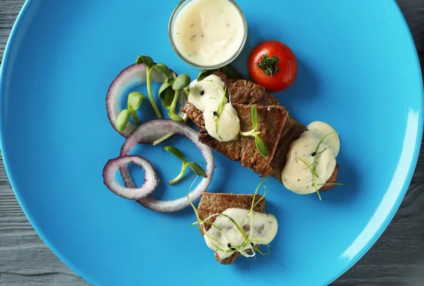 Bife fatiado servido com legumes e molho branco no prato azul — Fotografia de Stock