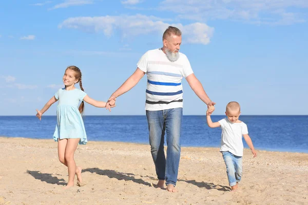 Cute children with grandfather on sea beach — Stock Photo, Image