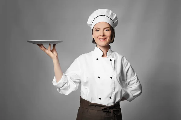 Vrouwelijke chef-kok met een leeg bord op grijze achtergrond — Stockfoto