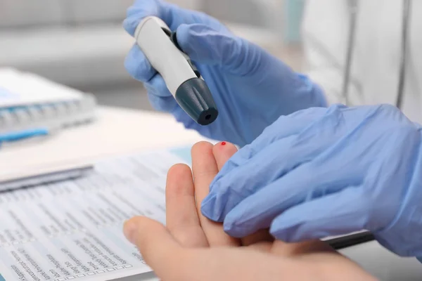 Técnico médico em luvas de látex recolhendo amostra de sangue de paciente com caneta lancet no hospital — Fotografia de Stock