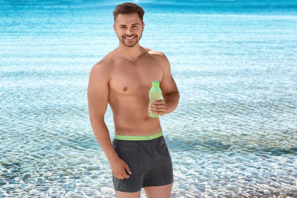 Junger schöner Mann mit Flasche Wasser am Strand — Stockfoto