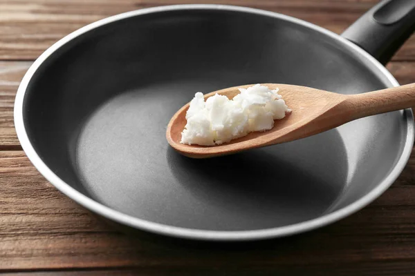 Cuchara de madera con aceite de coco en sartén sobre mesa —  Fotos de Stock