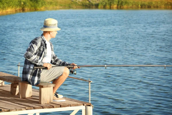 Young man fishing from pier on river — Stock Photo, Image