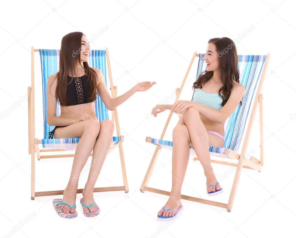 Beautiful young women sitting on deck chairs against white background
