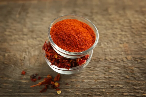 Chili powder and flakes in bowls on wooden table — Stock Photo, Image