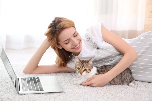 Ung vacker kvinna med katt och laptop på mattan hemma — Stockfoto