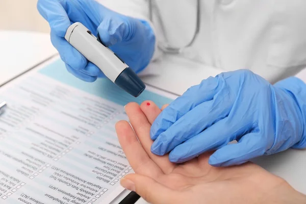 Medical technician in latex gloves taking blood sample of patient with lancet pen in hospital — Stock Photo, Image